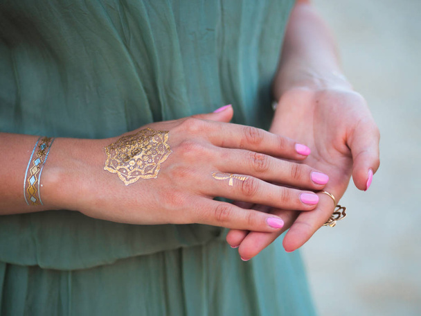Silver and golden flash tattoo on female hands over sea or ocean background. close up hands with boho gypsy gold accessories. Woman standing on the beach at summer - Fotó, kép