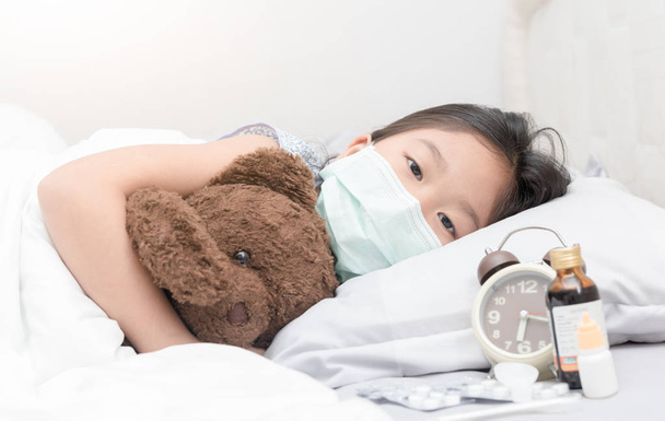 Menina doente com máscara higiênica que coloca na cama
 - Foto, Imagem