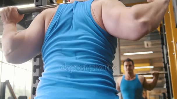 Fitness gym - muscular man performs squats with barbell - rear view - Πλάνα, βίντεο