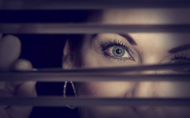 Portrait of a woman standing in darkness looking through blinds  - Foto, Bild