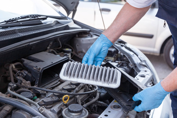 Auto mechanic wearing protective work gloves holds a dirty air filter - Foto, immagini