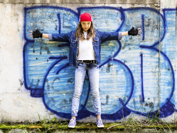 Милая молодая светловолосая девочка-подросток в бейсболке и джинсовой рубашке на фоне каменной стены
. - Фото, изображение