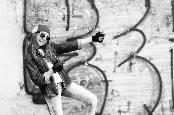Linda joven adolescente de pelo justo en una gorra de béisbol y camisa de mezclilla en un fondo de pared de piedra. BW
 - Foto, Imagen