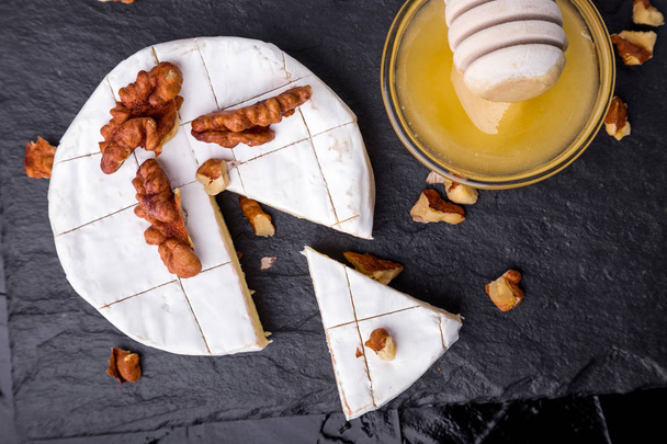 Sýr hermelín s ořechy a o honyey na pozadí černé břidlicové desky. Pohled shora. - Fotografie, Obrázek