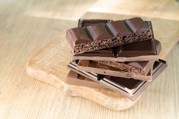 Διαφορετικές σπασμένες Μπάρες σοκολάτας στοιβάζονται σε ξύλινη σανίδα. Σοκολάτα, φωτίζονται από τον ήλιο. Θέση για το κείμενο.  - Φωτογραφία, εικόνα