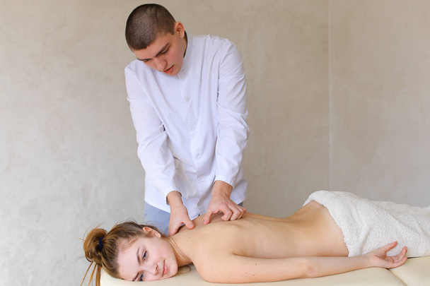 Красивый мужчина-ортопед делает массаж спины женщине, которая лежит
 - Фото, изображение