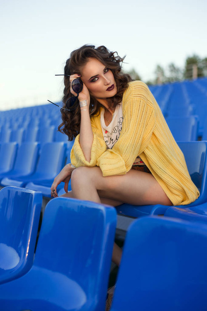 beautiful girl sits at stadium on a blue seats - Φωτογραφία, εικόνα
