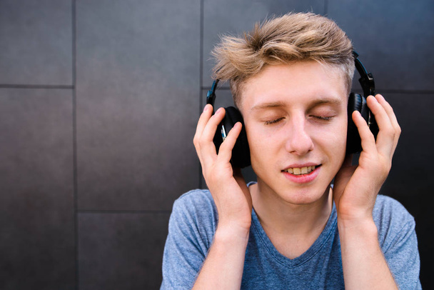 Πορτρέτο του ένας χαμογελαστός νεαρός με τα μάτια του κλειστά, απολαμβάνοντας τη μουσική με τα ακουστικά του. Ο τύπος βουίζει μουσική από τα ακουστικά. - Φωτογραφία, εικόνα
