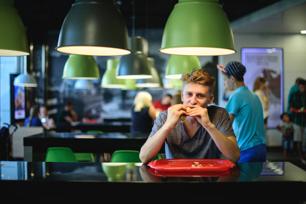 Student greedily eats a great beautiful burger sitting in a fast food restaurant. - Photo, Image
