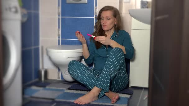 vrouw zittend op de vloer in de badkamer bezit zwangerschapstest met twee strepen - Video