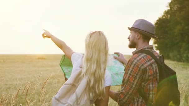 Happy traveling young people choose a route on the map against the backdrop of the sunrise in a spacious field. - Imágenes, Vídeo