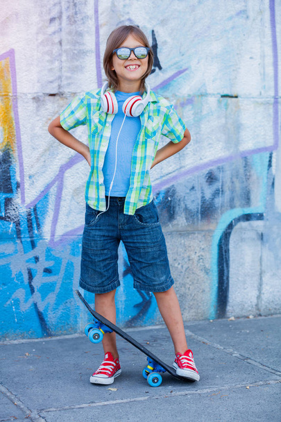Cute boy with skateboard outdoors, standing on the street with different colorful graffiti on the walls - Φωτογραφία, εικόνα