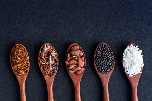 collection of grains in wooden spoon on black background. - Foto, Imagen