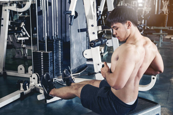 Fitness young man exercising using rowing machine in the gym - Foto, imagen