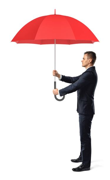 A businessman in side view holds an open red umbrella in both hands in front of him. - Fotografie, Obrázek