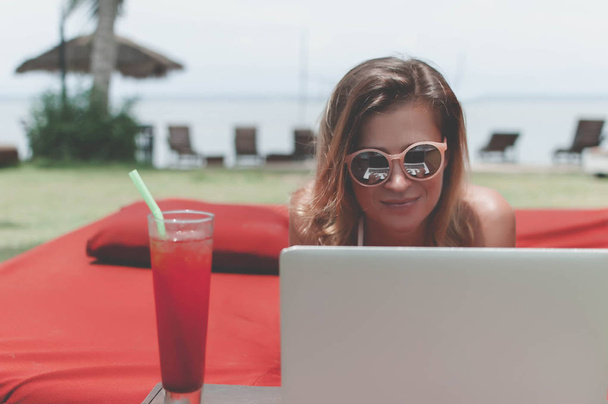 Young female freelancer laying near the pool and working on her laptop. - 写真・画像
