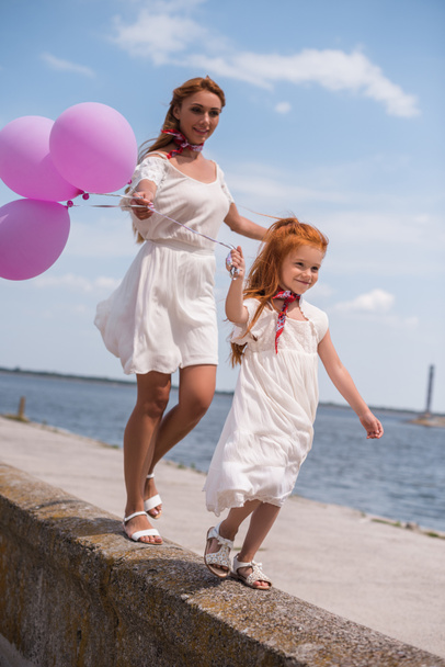 mother and daughter with balloons at seashore - Foto, imagen