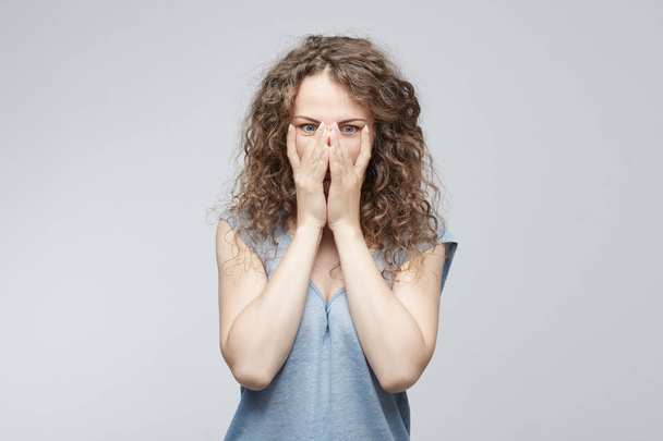  Разочарованная депрессивная женщина с волосяной булочкой в голубой свободной футболке, покрывающей лицо усталыми и измученными руками. Отчаянная женщина с депрессией скрывает плачущее лицо руками
 - Фото, изображение