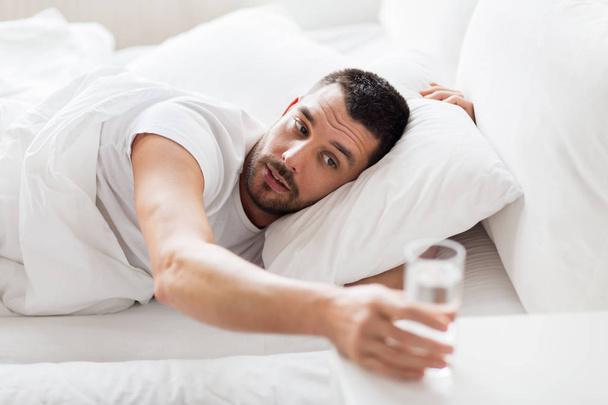 man in bed and reaching to glass of water at home - Photo, image