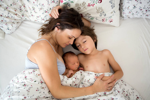 Young mother lying in bed with her newborn baby boy and his olde - Foto, imagen