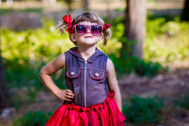 Portret van mooie kleine meisje model in zonnebril in bogen in een park - Foto, afbeelding