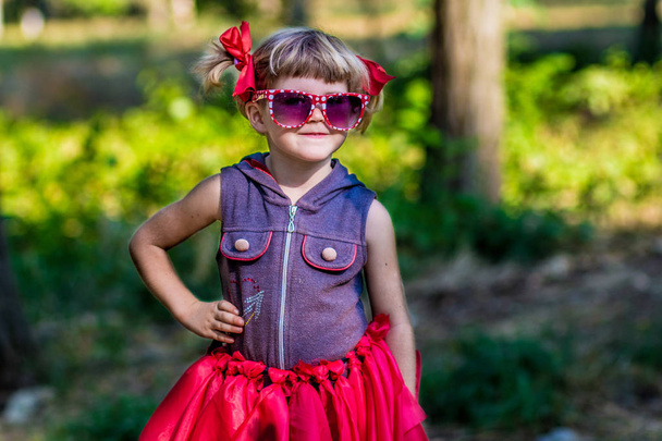 Porträt der schönen kleinen Mädchen Modell mit Sonnenbrille in Schleifen in einem Park - Foto, Bild