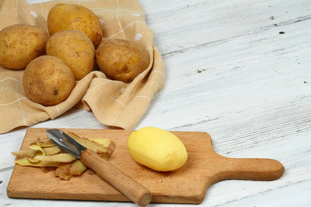 Obieranie surowe ziemniaki z skrobak stary na biały stół - Zdjęcie, obraz