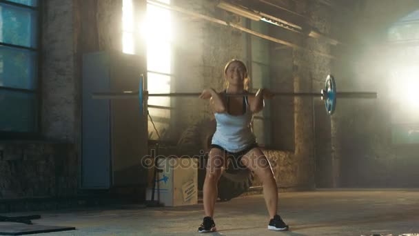 Strong Athletic Woman in Sportswear Lifts Heavy Barbell and Does Squats with it as a Part of Her Cross Fitness Training Routine. Gimnasio está en fábrica remodelada
. - Imágenes, Vídeo