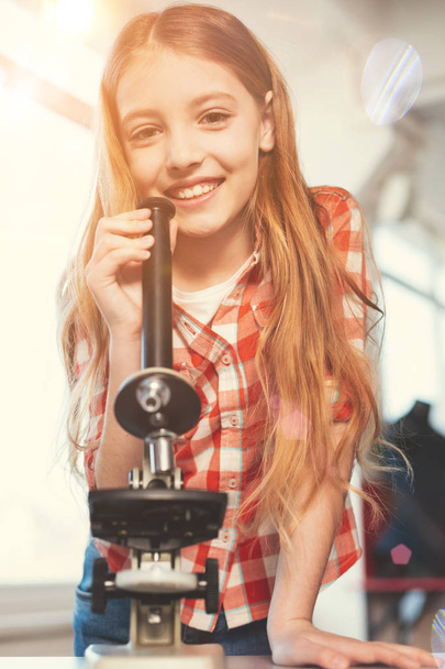 Positiivinen iloinen tyttö poseeraa mikroskoopilla
 - Valokuva, kuva