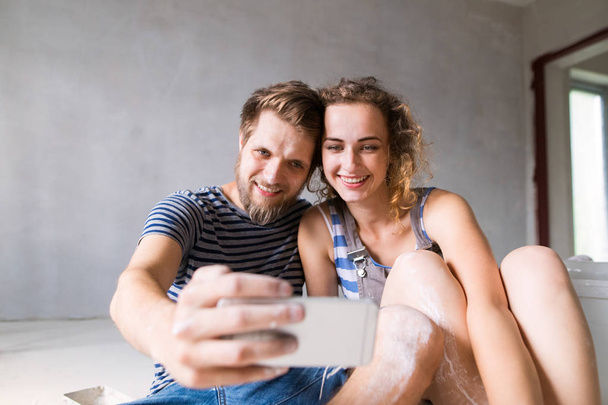 Couple at home painting walls, taking selfie with smartphone. - Φωτογραφία, εικόνα