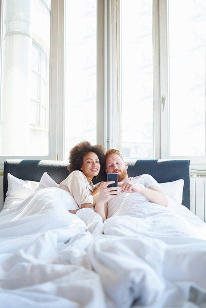 couple watching video on phone in bed - Φωτογραφία, εικόνα