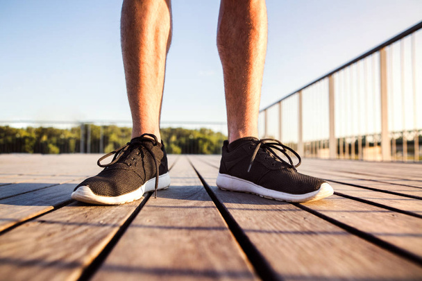 Legs of unrecognizable runner standing on wooden bridge. - Zdjęcie, obraz
