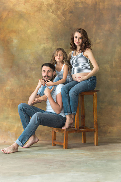 Pregnant mother with teen daughter and husband. Family studio portrait over brown background - Фото, зображення