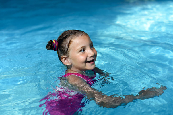 A little girl swimming in a bright turquoise water of a pool   - Photo, Image