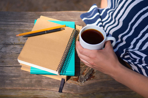 a girl holds a cup of coffee and sits on a park bench. Notebooks for writing and books. Studies, work and business concept - Foto, immagini