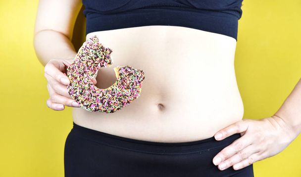 Dikke vrouw uit zoete donut en slechte junkfood, middelbare leeftijd vrouw met buitensporige buik vet, vrouw muffin top taille overgewicht. - Foto, afbeelding