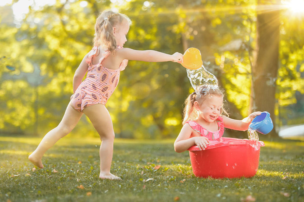 The cute little blond girls playing with water splashes on the field in summer - Fotoğraf, Görsel