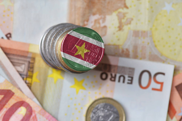 монета евро с национальным флагом Суринама на фоне банкнот евро
. - Фото, изображение