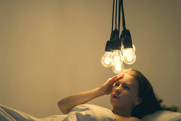 A girl lies in bed under big light bulbs can't fall asleep. Concept picture. Insomnia. Psychology.  - Foto, Imagem