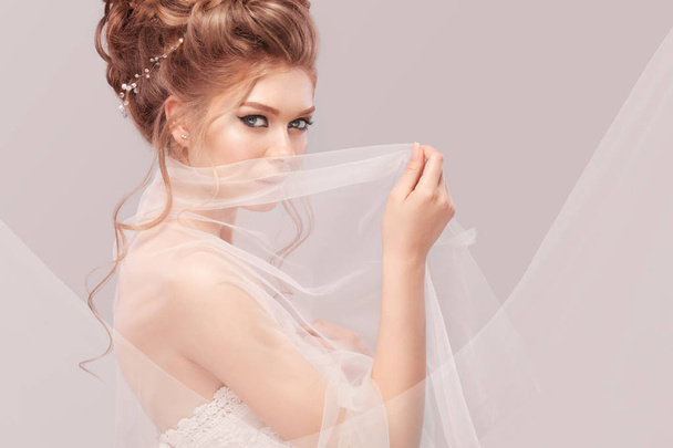 Beautiful bride with fashion wedding hairstyle - on gray background. Closeup portrait of young gorgeous bride. Wedding. Studio shot with copy space. Beautiful bride portrait with veil over her face - Φωτογραφία, εικόνα