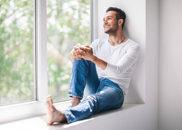 smiling man relaxing on window sill - Фото, изображение