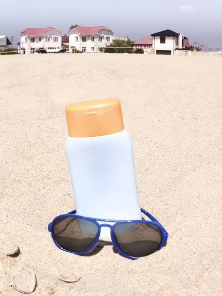 Пляшка бальзаму сонячна з мушлями та сонцезахисними окулярами на піску
 - Фото, зображення