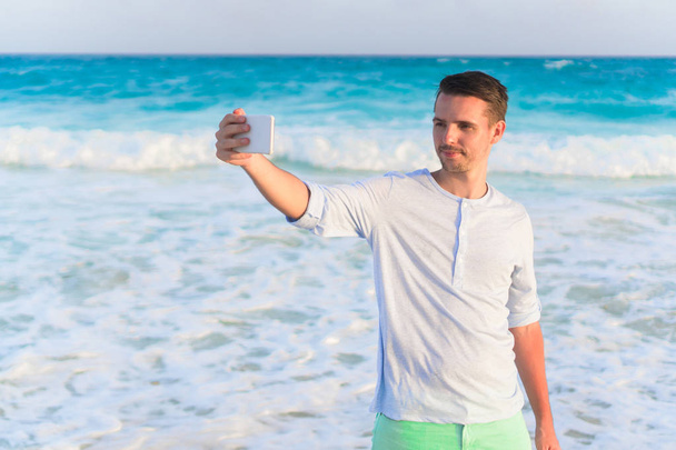 Молодой человек делает селфи на пляже на фоне моря
 - Фото, изображение