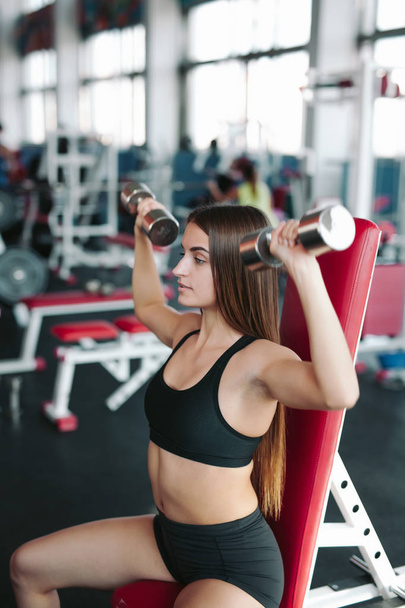 Fit woman 20s doing shoulder raises with dumbbells in gym - Foto, afbeelding