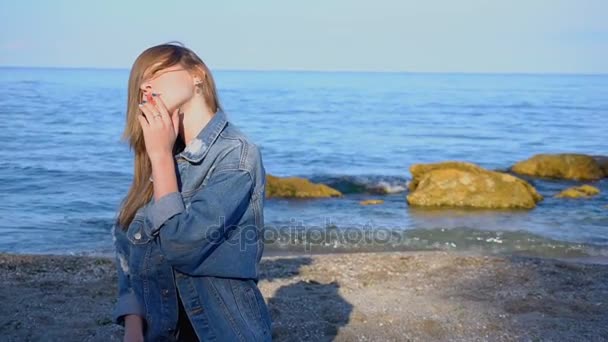 Krásná dívka šla na břehu Černého moře, usmíval se a koukal, stojící na pláži na chladné letní den. - Záběry, video