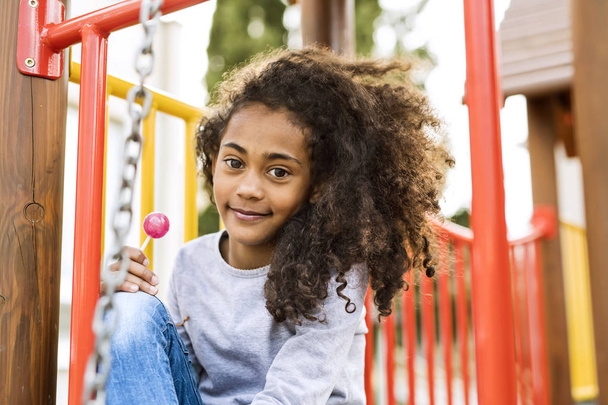 African american girl on playground eating lollipop. - Фото, зображення