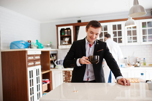 Portrait of a handsome groom drinking coffee in the kitchen. - 写真・画像