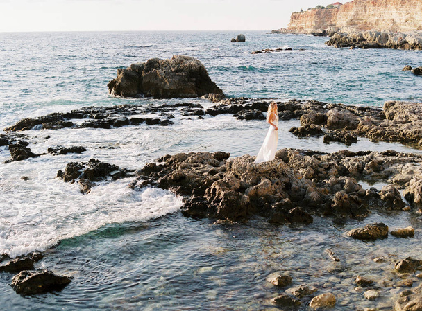 Blond bride posing on rocks near the sea. Delicate and sincere photos. Wedding abroad. Wedding on the beach - Foto, imagen