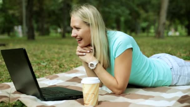 草の上のラップトップを持つ若い女性。少女が公園でノート パソコンを使って skype で話しています。. - 映像、動画