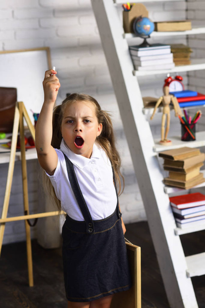 Girl with angry face near school supplies and bookshelf - Φωτογραφία, εικόνα